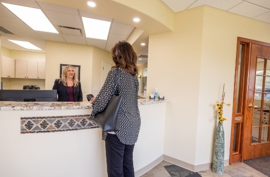 Dental office receptionist at front desk talking to a patient