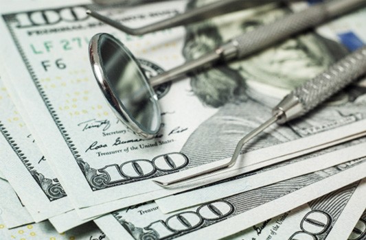 Dental tools lying on a pile of hundred-dollar bills