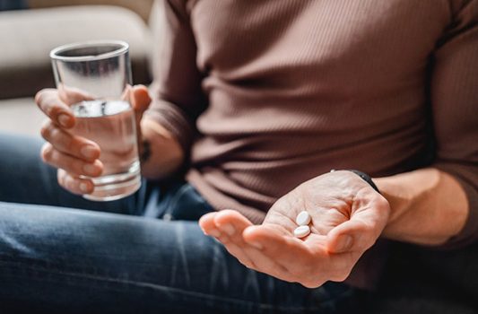 Man holding two tablets of OTC pain relievers and a glass of water