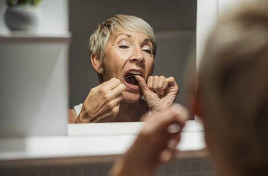 Woman flossing her teeth in bathroom mirror